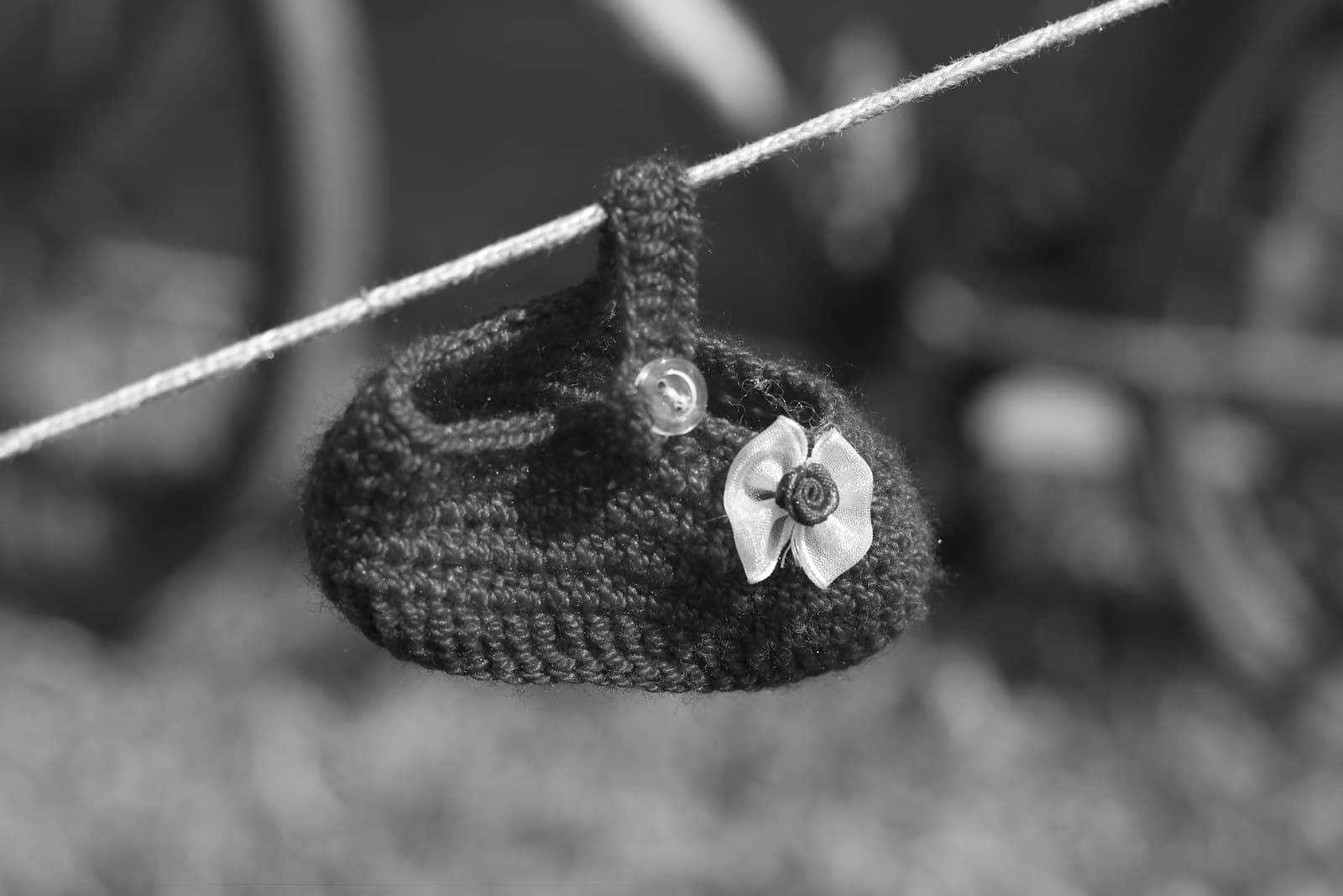A small black crocheted baby bootie with a white flower detail, hanging from a clothesline