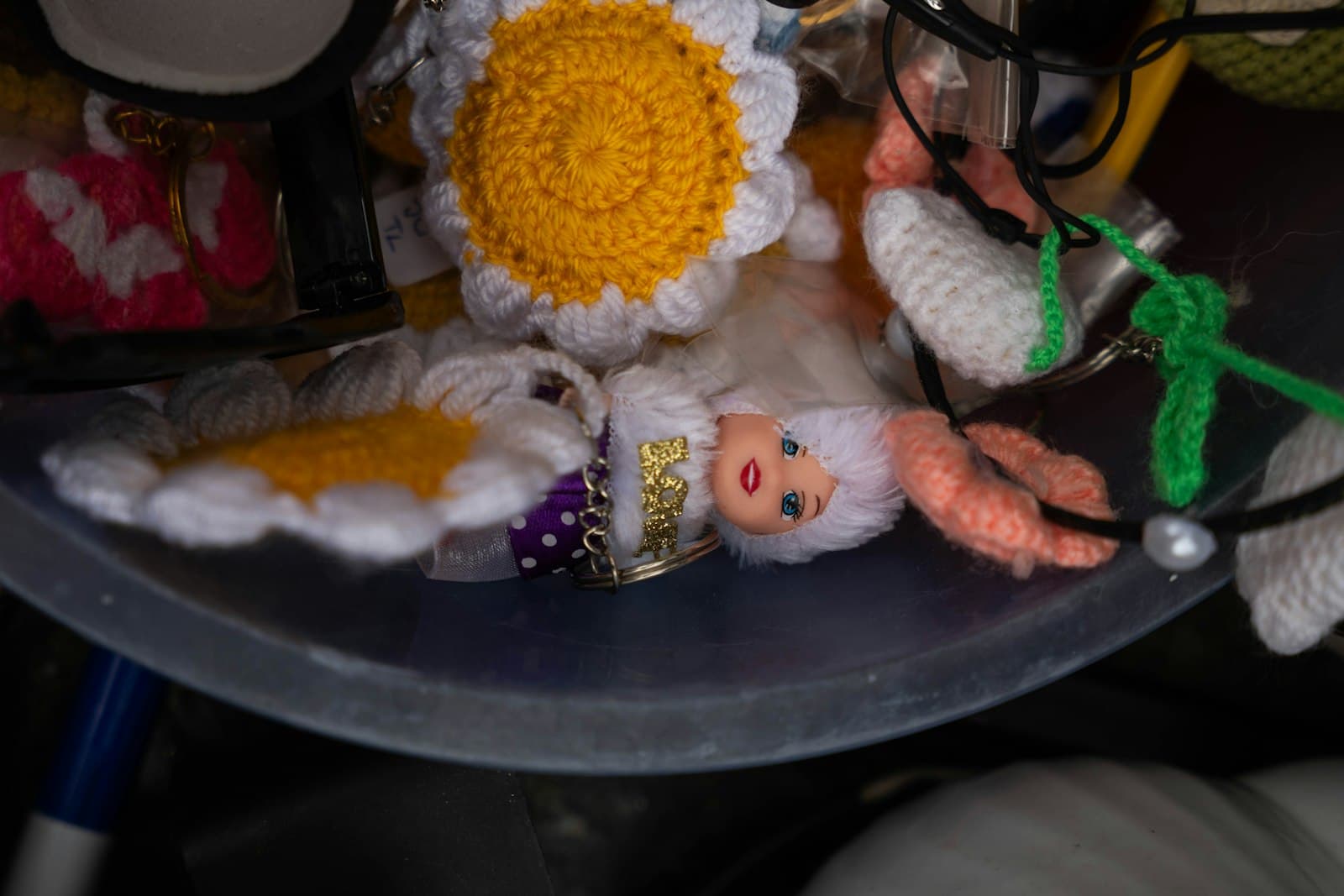 A handmade crocheted daisy flower keychain in white and yellow, alongside small crochet trinkets