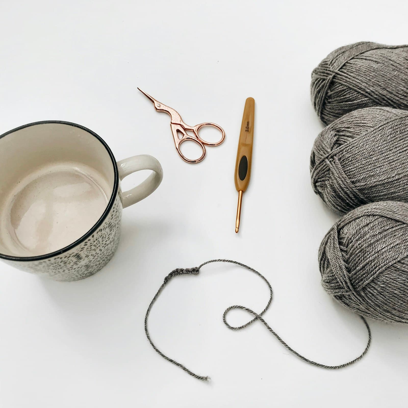 A cup of yarn with scissors, hooks, and other crochet tools on a table
