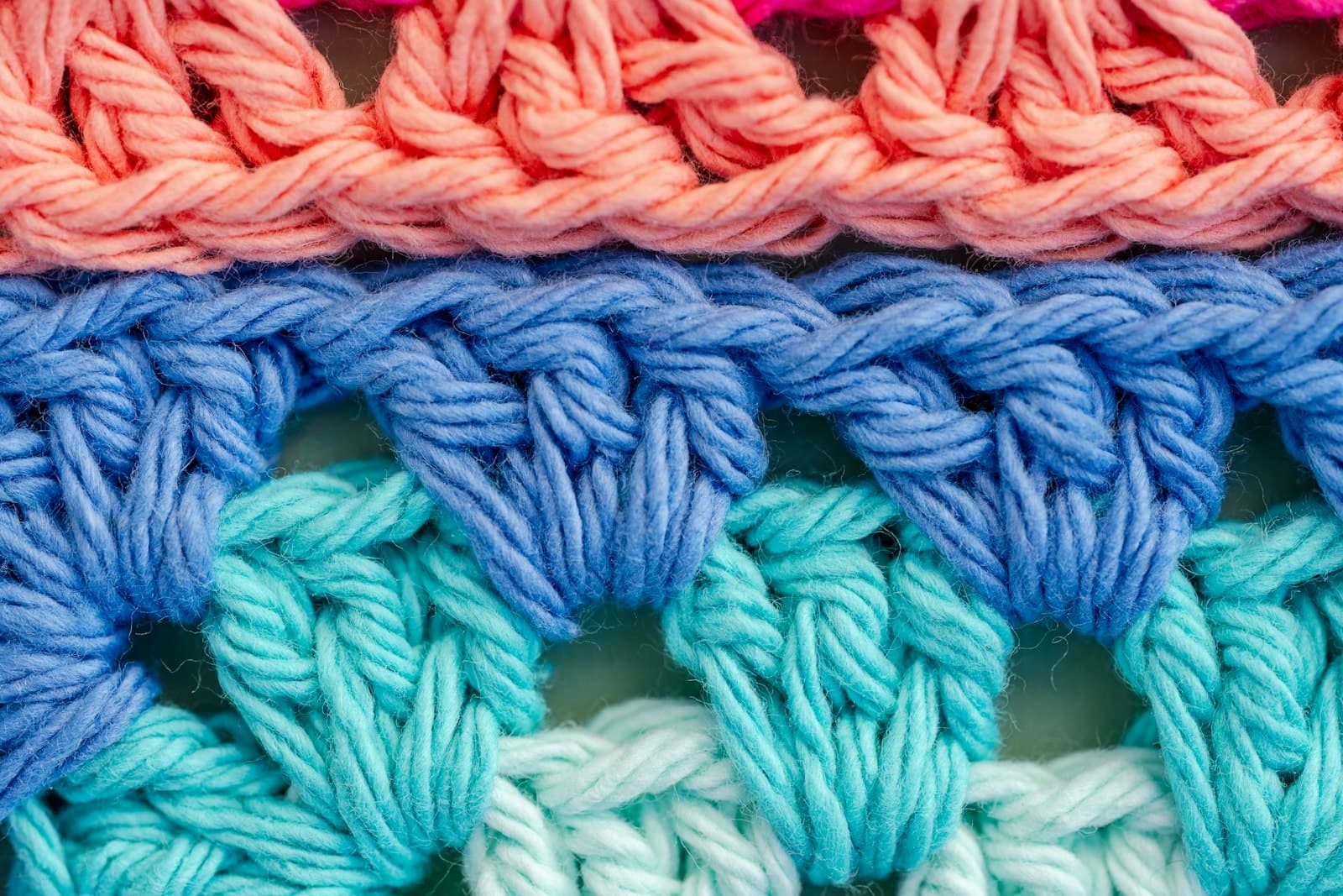 Close-up of colorful crocheted stitches in coral, blue, and teal showing the V-shaped texture of double crochet